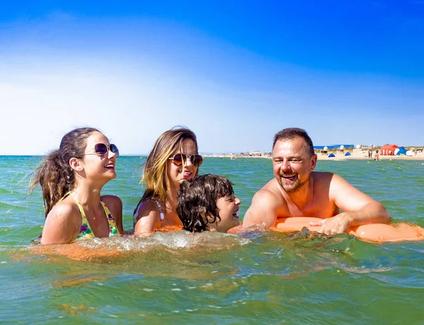 Gelukkig gezin van vier in de vakantie op zee kust. Gelukkige familie met gele matras baadt in zee. Gelukkig moeder Papa en twee kinderen spelen in het water — Stockfoto