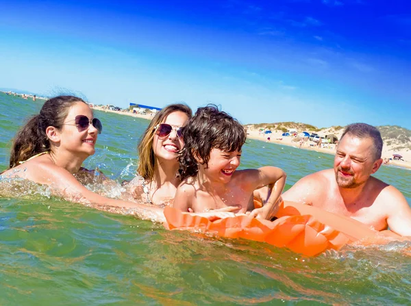 Famiglia felice di quattro in vacanza sulla riva del mare. Famiglia felice con materasso giallo bagna in mare. felice mamma papà e due bambini giocano in acqua — Foto Stock