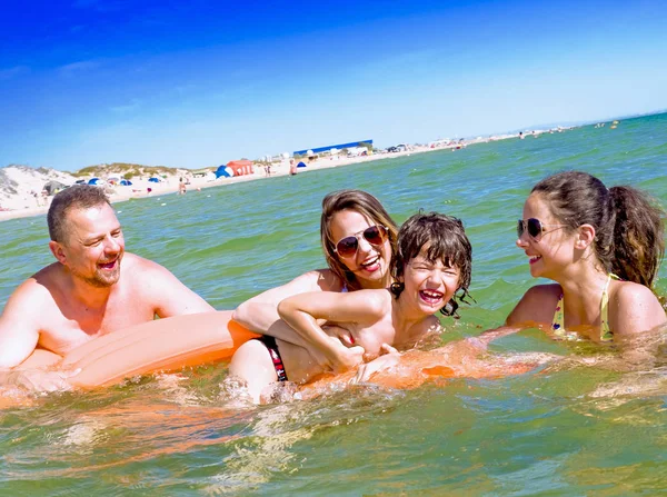 Gelukkig gezin van vier in de vakantie op zee kust. Gelukkige familie met gele matras baadt in zee. Gelukkig moeder Papa en twee kinderen spelen in het water — Stockfoto