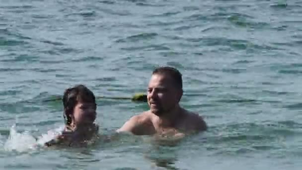 Μπαμπάς και γιος αναπαύονται πάνω στη θάλασσα. Ο μπαμπάς διδάσκει τον γιο του να κολυμπήσετε. — Αρχείο Βίντεο