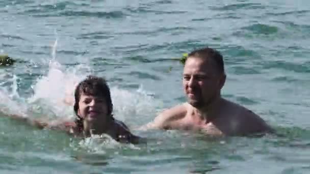 Dad and son are resting on the sea. Dad teaches his son to swim. — Stock Video