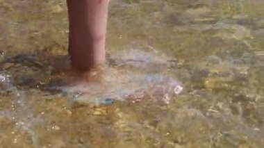 Yaz tatilinde tropik kumsalda bir kız ayaklarını berrak deniz suyuna daldırıyor..