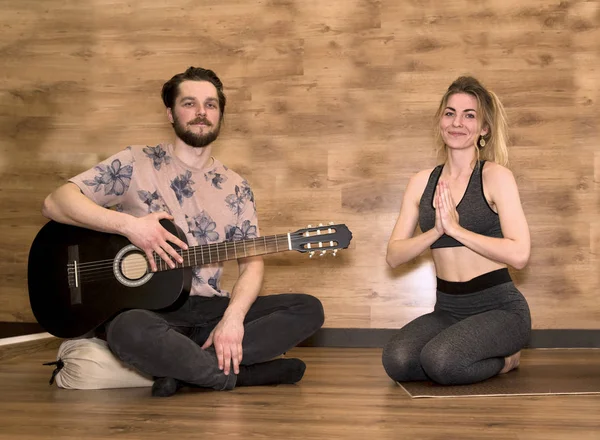 Newlyweds yoga meditation. Man playing guitar, woman doing asana exercises.