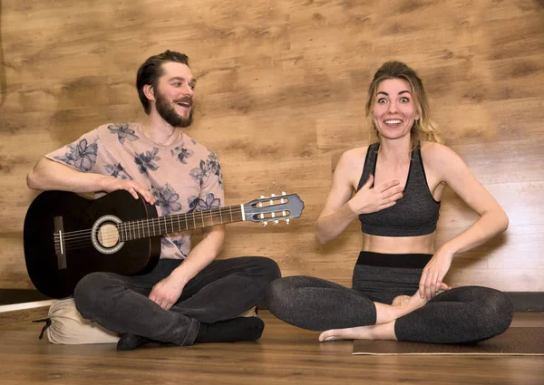Newlyweds yoga meditation. Man playing guitar, woman doing asana exercises.