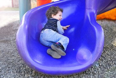 Bir çocuk oyun alanı üzerinde küçük bir çocuk bir tepe üzerinde sürmek.