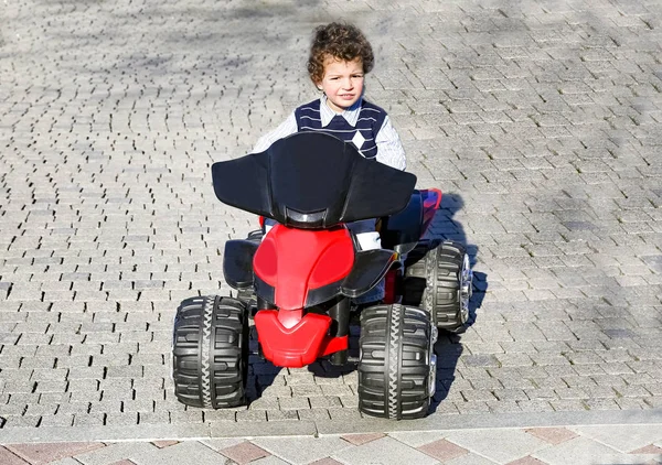 Garçon de quatre ans en chemise rayée dans une voiture jouet rouge dans la rue — Photo