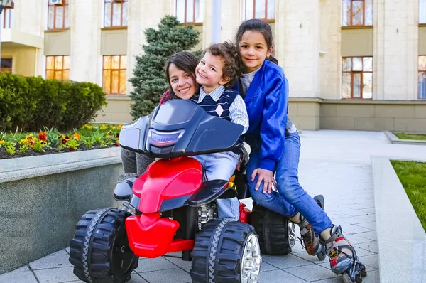 Kids driving electric toy car in summer park. Outdoor toys. Children in battery power vehicle. Little boy and his two older sisters are riding a toy truck in the city. Affection and fun time concept