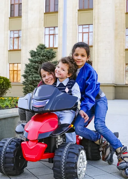 Kids driving electric toy car in summer park. Outdoor toys. Children in battery power vehicle. Little boy and his two older sisters are riding a toy truck in the city. Affection and fun time concept