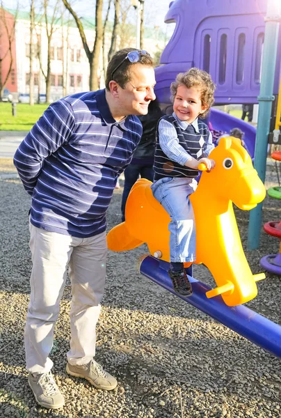 Father and son having fun on swing at playground in park — Stock Photo, Image