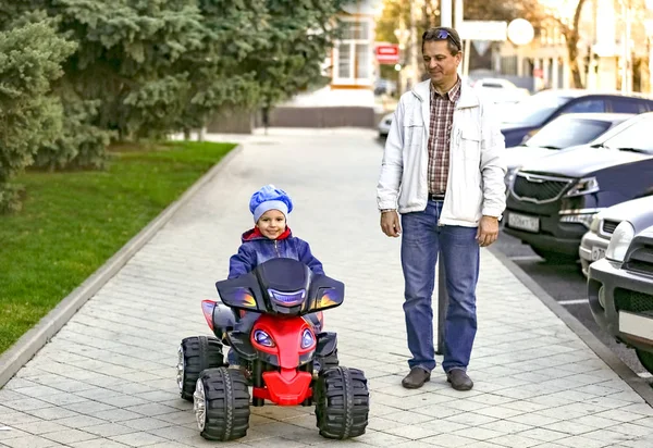 Dad with his son for a walk. Happy family in the city park. The concept of a happy family. Little boy driving an electric car.