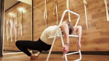 Studio ahşap duvarlar ve zemin ile pratik yoga öğretmeni. Yogi sandalye için parsvottanasana poz kullanarak. Duruş, yavaş yardım etmek Iyengar yoga eğitmeni ile sandalye pervane gibi