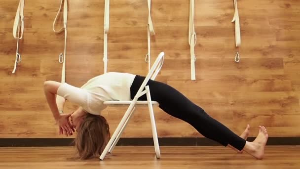 Yogalehrer beim Üben im Studio mit Holzwänden und Fußboden. Yogi mit Stuhl für parsvottanasana Pose. Iyengar Yogalehrer mit Stuhl als Stütze, um in Haltung, Zeitlupe zu helfen — Stockvideo