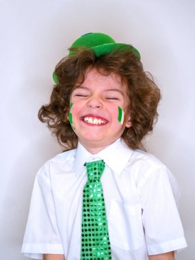 İspanyol çocuk çocuk eğleniyor Saint Patrick kutlamalar sırasında hafif bir arka plan üzerinde. Yanağımın üstünde Yeşil yonca ve İrlanda bayrağı bir çocuk gülümsüyorum. Aziz Patrick günü kutlamaları.