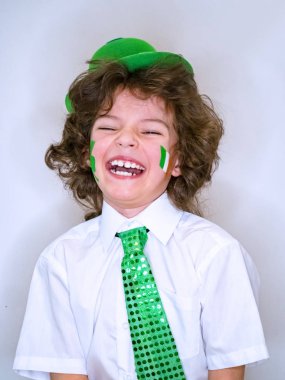 İspanyol çocuk çocuk eğleniyor Saint Patrick kutlamalar sırasında hafif bir arka plan üzerinde. Yanağımın üstünde Yeşil yonca ve İrlanda bayrağı bir çocuk gülümsüyorum. Aziz Patrick günü kutlamaları.