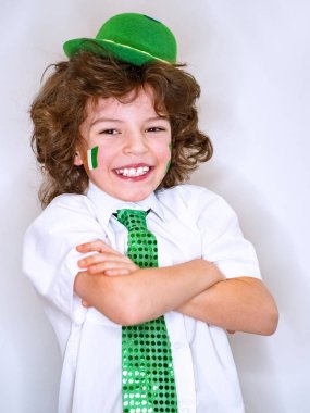 İspanyol çocuk çocuk eğleniyor Saint Patrick kutlamalar sırasında hafif bir arka plan üzerinde. Yanağımın üstünde Yeşil yonca ve İrlanda bayrağı bir çocuk gülümsüyorum. Aziz Patrick günü kutlamaları.
