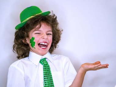 Kıvırcık çocuk çocuk eğleniyor Saint Patrick kutlamalar sırasında hafif bir arka plan üzerinde. Yeşil bir yonca çocukla yanağımda hayali bir konu benim elinde tutan gülümsüyorum zaten. Kopya alanı