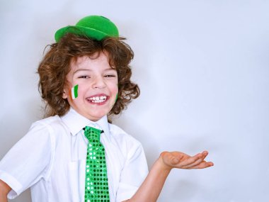 Saint Patrick celebrations over a light background. I am a smiling boy with a Irish flag on my cheek holding an imaginary subject in my hand. Copy space clipart