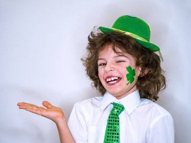 Kıvırcık çocuk çocuk eğleniyor Saint Patrick kutlamalar sırasında hafif bir arka plan üzerinde. Yeşil bir yonca çocukla yanağımda hayali bir konu benim elinde tutan gülümsüyorum zaten. Kopya alanı