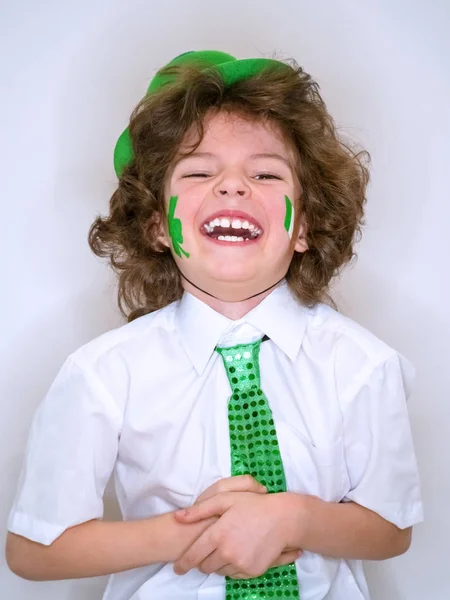 Hispanic kind jongen plezier tijdens Saint Patrick feesten op een lichte achtergrond. Ik ben een jongen met een groene klaver en de Ierse vlag lachend op mijn Wang. Patrick's Day vieringen. — Stockfoto