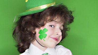 Çocuk kutlayan St. Patrick's günü onun makyaj gösterilen. Bir küçük, düzgün vücutlu erkek onun yanağına bir yaprak yonca ve İrlanda bayrağı şeklinde bir çizim, onun parmak işaret eder. ağır çekim. yeşil arka plan
