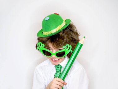 Komik St Patricks günü yeşil bir şapka, karnaval gözlük ve bir kravat giyen küçük çocuk çarpıcı. Kıvırcık çocuk büyük yeşil kalem hafif bir arka plan üzerinde el ile poz