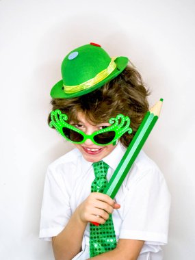 Komik St Patricks günü yeşil bir şapka, karnaval gözlük ve bir kravat giyen küçük çocuk çarpıcı. Kıvırcık çocuk büyük yeşil kalem hafif bir arka plan üzerinde el ile poz