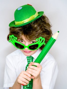 Komik St Patricks günü yeşil bir şapka, karnaval gözlük ve bir kravat giyen küçük çocuk çarpıcı. Kıvırcık çocuk büyük yeşil kalem hafif bir arka plan üzerinde el ile poz