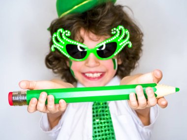 Komik St Patricks günü yeşil bir şapka giymiş küçük çocuk çarpıcı. Dişlek bir gülümseme yanıp sönen kıvırcık çocuk onun elinde büyük bir yeşil kalem ile poz. açık renkli
