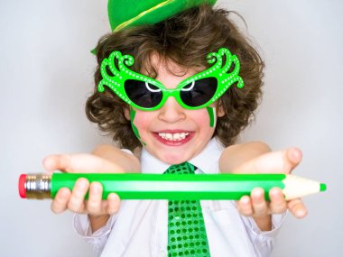 Komik St Patricks günü yeşil bir şapka giymiş küçük çocuk çarpıcı. Dişlek bir gülümseme yanıp sönen kıvırcık çocuk onun elinde büyük bir yeşil kalem ile poz. açık renkli