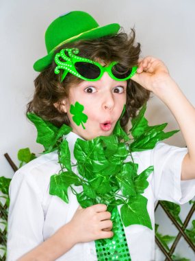 Komik St Patricks günü yeşil karnaval aksesuarları ve yeşil bir şapka giymiş küçük kıvırcık çocuk açık ağzı ile şok. açık renkli