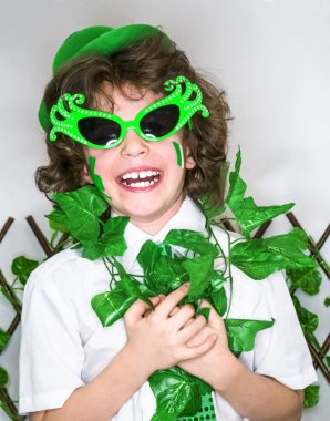 Çocuk kutlayan St. Patrick's günü onun makyaj gösterilen. Bir küçük, kıvırcık boy gülümseyerek kameraya bakarak yeşil karnaval aksesuarları. yeşil arka plan