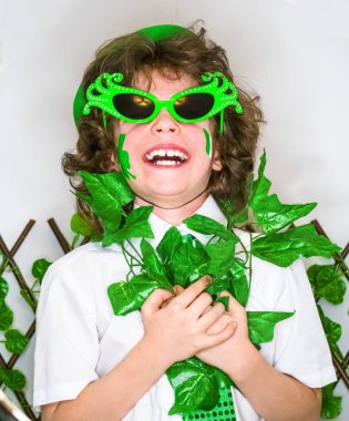 Çocuk kutlayan St. Patrick's günü onun makyaj gösterilen. Bir küçük, kıvırcık boy gülümseyerek kameraya bakarak yeşil karnaval aksesuarları. yeşil arka plan