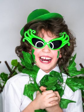 Çocuk kutlayan St. Patrick's günü onun makyaj gösterilen. Bir küçük, kıvırcık boy gülümseyerek kameraya bakarak yeşil karnaval aksesuarları. yeşil arka plan