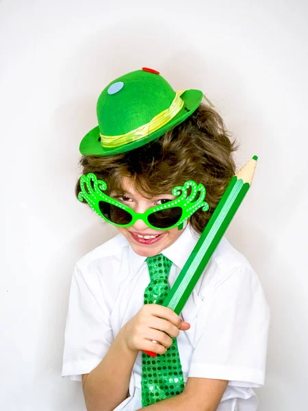 Komik St Patricks günü yeşil bir şapka, karnaval gözlük ve bir kravat giyen küçük çocuk çarpıcı. Kıvırcık çocuk büyük yeşil kalem hafif bir arka plan üzerinde el ile poz