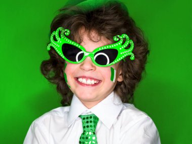 Çocuk kutlayan St. Patrick's günü onun makyaj gösterilen. Bir küçük, kıvırcık boy gülümseyerek kameraya bakarak yeşil karnaval aksesuarları. yeşil arka plan