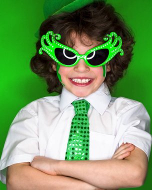 Çocuk kutlayan St. Patrick's günü onun makyaj gösterilen. Bir küçük, kıvırcık boy gülümseyerek kameraya bakarak yeşil karnaval aksesuarları. yeşil arka plan