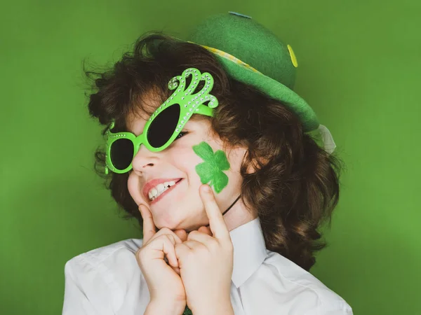 Çocuk kutlayan St. Patrick's günü onun makyaj gösterilen. Yeşil karnaval aksesuarları küçük bir kıvırcık çocuk parmaklarını formu shamrock çizimde, onun cheek.green arka plan üzerinde Puan