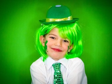 Çocuk kutlayan St. Patrick's günü onun makyaj gösterilen. Küçük bir gülümseyen çocuk yeşil karnaval aksesuarları kameraya bakıyor. yeşil arka plan