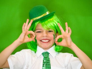Çocuk kutlayan St. Patrick's günü onun makyaj gösterilen. Bir küçük, düzgün vücutlu shamrock ve çocuk bir jest iyi gösterilen yanakları İrlanda bayrağı. ağır çekim. yeşil arka plan