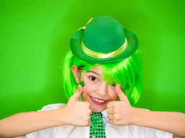Çocuk kutlayan St. Patrick's günü onun makyaj gösterilen. Bir küçük, düzgün vücutlu shamrock ve çocuk bir jest iyi gösterilen yanakları İrlanda bayrağı. ağır çekim. yeşil arka plan