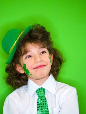 Sevimli çocuk çocuk eğleniyor Saint Patrick kutlamalar sırasında yeşil bir arka plan üzerinde. Shamrock yanağında küçük bir çocuk. Ararken bir çocuk. Aziz Patrick günü kutlamaları.