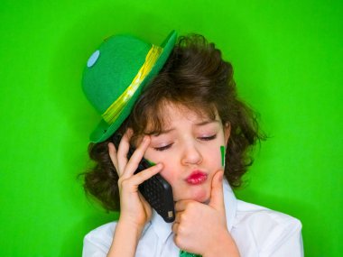 Küçük çocuk bir yeşil şapka ve yonca, telefonda konuşurken onun yanaklarda İrlanda bayrağı çarpıcı komik St Patricks Günü. Ciddi ve düşünceli çocuk haber telefon dinleme
