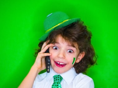Komik St Patricks Günü küçük çocuk bir yeşil şapka ve yonca, telefonda konuşurken onun yanaklarda İrlanda bayrağı giyiyor. Son derece heyecanlı ve eğlenceli bir çocuk için iyi haber telefon dinleme