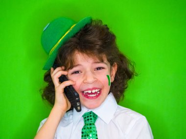 Komik St Patricks Günü küçük çocuk bir yeşil şapka ve yonca, telefonda konuşurken onun yanaklarda İrlanda bayrağı giyiyor. Son derece heyecanlı ve eğlenceli bir çocuk için iyi haber telefon dinleme