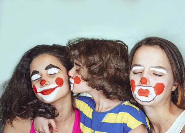 Twee tiener zusjes en een broertje in de rol van clowns poseren in de studio. Jaloezie concept. — Stockfoto