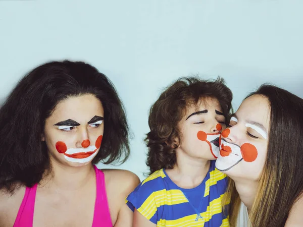 Twee tiener zusjes en een broertje in de rol van clowns poseren in de studio. Jaloezie concept. — Stockfoto