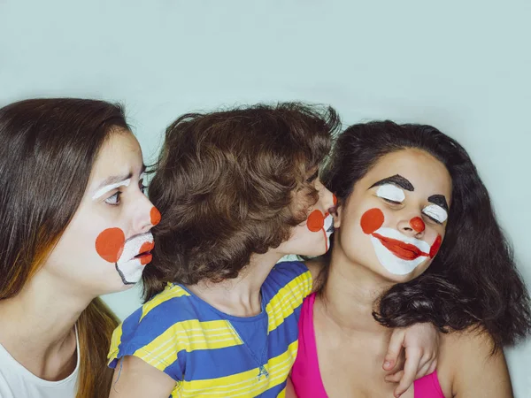 Twee tiener zusjes en een broertje in de rol van clowns poseren in de studio. Jaloezie concept. — Stockfoto