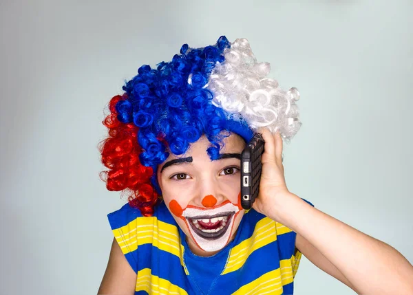 Portret van gelukkig grappige clown kind houden smartphone en genieten van goed nieuws. Positieve en expressie concept. Geïsoleerd op gray.pantomimic expressie. emoties. April Fool's Day, 1 April — Stockfoto