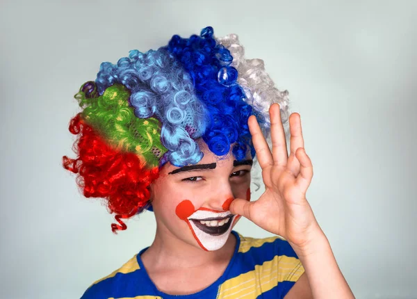 Little Cute Boy en peluca y cara pintada en broma muestra su larga nariz con los dedos de la palma de la mano. Aislado en gris . — Foto de Stock