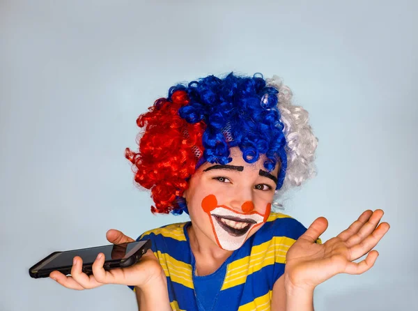 Portret van gelukkig grappige clown kind houden smartphone en genieten van goed nieuws. Positieve en expressie expressie van de concept.pantomimic. emoties. April Fool's Day, 1 April. Geïsoleerd op grijs. — Stockfoto